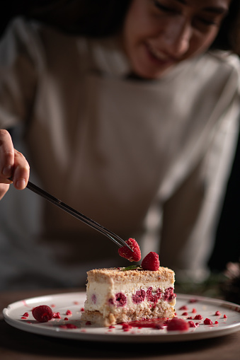 A female chef decorating a cheesecake with a strawberry for Christmas dinner.