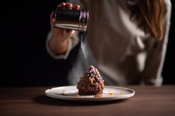 A female chef finishing a pine tree-like chestnut tart A female chef finishing a pine tree-like chestnut tart for Christmas dinner with powdered sugar. sprinkling powdered sugar stock pictures, royalty-free photos & images