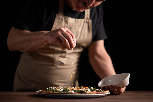 A male chef decorating a pizza.
