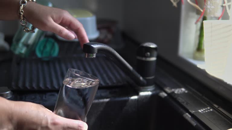 Pouring a glass of fresh water from a kitchen faucet in the black sink, closeup