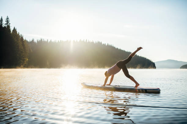 Young man making his morning yoga practice on a SUP board in the middle of a lake.