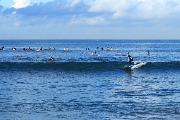 A surfer riding a beach break wave at Batu Bolong Beach in Canggu, Bali, Indonesia with other surfers waiting for waves in the background. A surfer riding a beach break wave at Batu Bolong Beach in Canggu, Bali, Indonesia with other surfers waiting for waves in the background. Batu Bolong is famous for riding long boards in Bali. kuta beach stock pictures, royalty-free photos & images