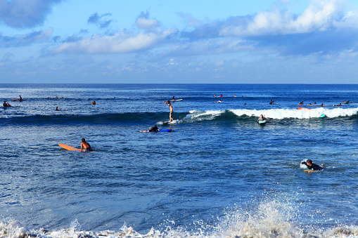 A surfer riding a beach break wave at Batu Bolong Beach in Canggu, Bali, Indonesia with other surfers waiting for waves in the background. Batu Bolong is famous for riding long boards in Bali.