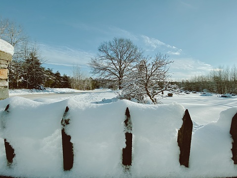 Iron fence with snow stuck on top and a beautiful Michigan landscape view peeking out from over the fence, taken from the road and drive leading into a Cemetery in Faithorn Township in The Upper Peninsula during a Polar Vortex winter storm. Sun and beautiful daytime skies above.