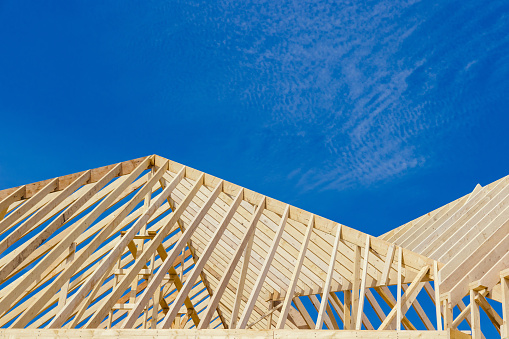 Low angle view of mature male carpenter holding tape measure while standing on wooden roof beam at construction site against sky