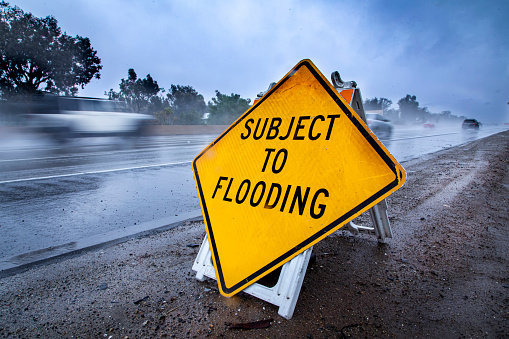 Road Sign stating Subject to Flooding with rainy highway in the bacground