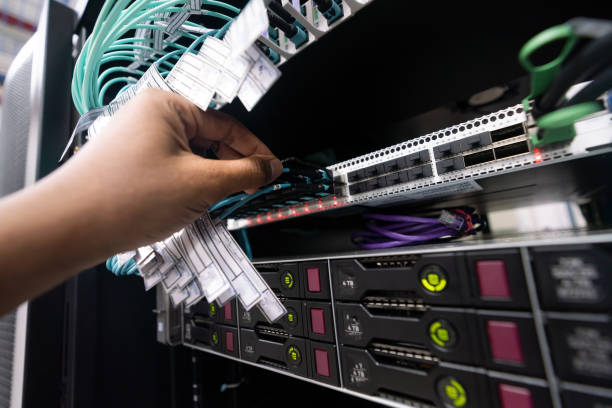 a close up of hand with fiber network cables connected to servers in a datacenter stock photo