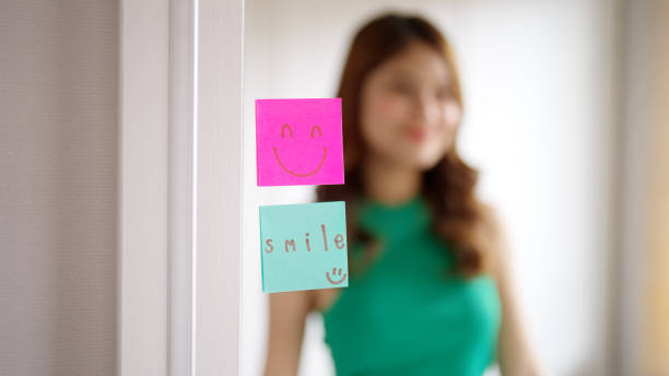 Asian woman self talk in front of mirror with smiley sticky note.