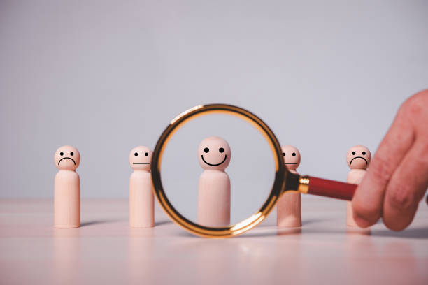 istock Male hand using a magnifying glass to look for a smiling wood cube person 1454520767