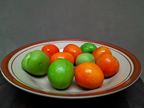 Some red tomatoes and green cucumbers on a brown ceramic plate