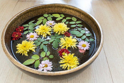 Pretty floating daisy flower petals and leaves on water in container as decoration present peaceful feeling