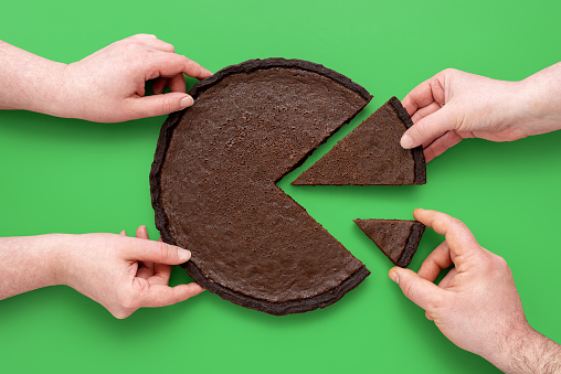 People hands taking slices of chocolate pie, above view on a green background. Unequal sharing the cake, concept for financial pie chart