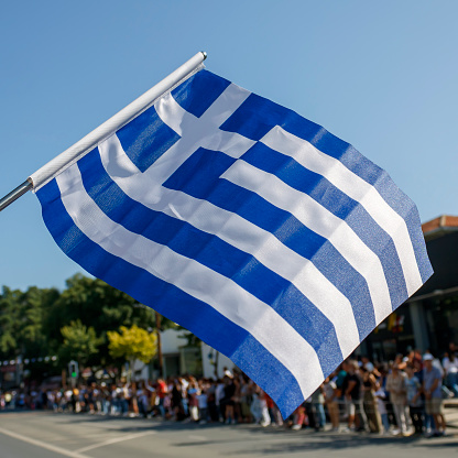 Greek flag waving on the street in front of parade spectators in Limassol, Cyprus