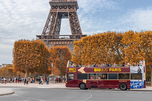 Big Bus carrying tourists driving in a street of Paris in Autumn and passing by the Eiffel Tower in France