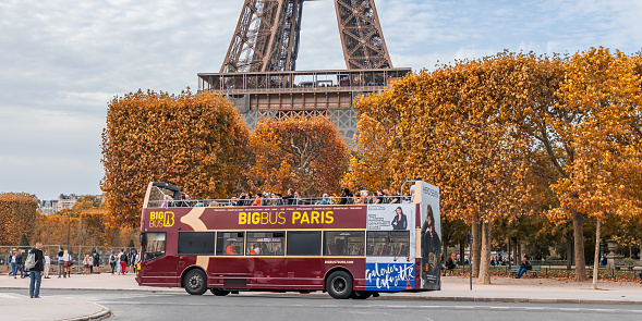 Big Bus carrying tourists driving in a street of Paris in Autumn and passing by the Eiffel Tower in France