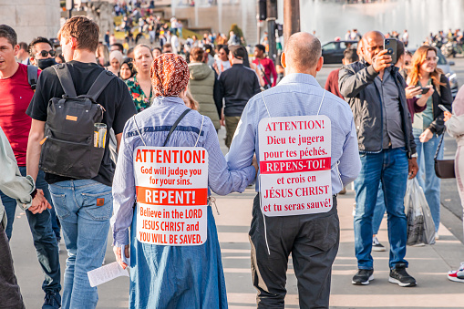 Couple of religious fanatics walking in a street in Paris and carrying signs asking to repent of our sins in France