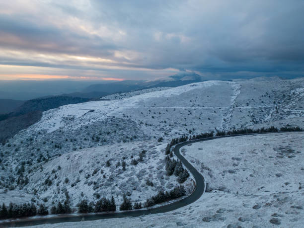 montañas cubiertas de nieve al atardecer con un camino sinuoso en primer plano vista aérea - road winding road mountain spiral staircase fotografías e imágenes de stock