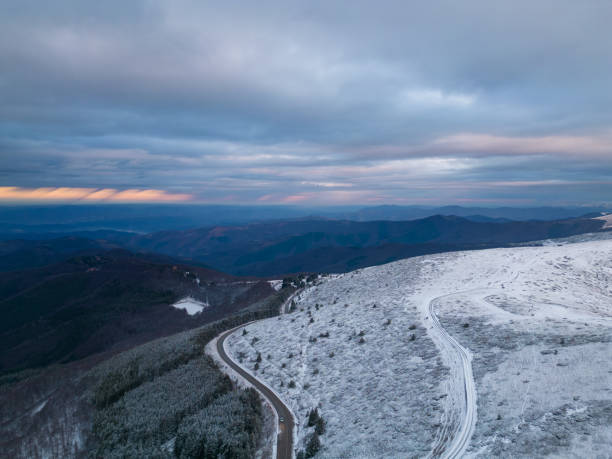 montañas cubiertas de nieve al atardecer con un camino sinuoso en primer plano vista aérea - road winding road mountain spiral staircase fotografías e imágenes de stock