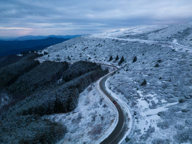 montañas cubiertas de nieve al atardecer con un camino sinuoso en primer plano vista aérea - road winding road mountain spiral staircase fotografías e imágenes de stock