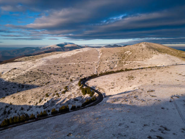 montañas cubiertas de nieve al atardecer con un camino sinuoso en primer plano vista aérea - road winding road mountain spiral staircase fotografías e imágenes de stock