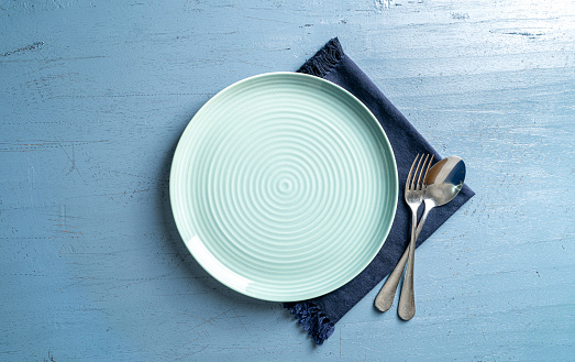 a top view of white plate with spoon and fork on a blue wood table