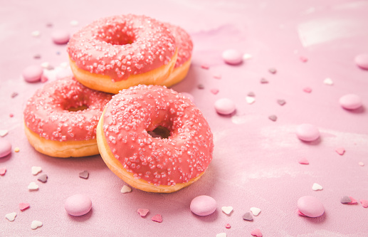 Pink donuts with sprinkles and pink chocolate beans on pink background