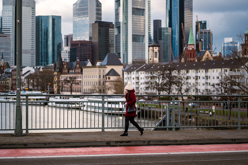 Frankfurt, Germany – November 27, 2021: A fashionable woman walking over a bridge with Frankfurt skyline background in Germany