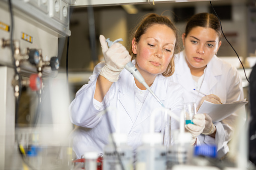 Focused female researchers mixing reagents in test tube with lab pipette while working in laboratory