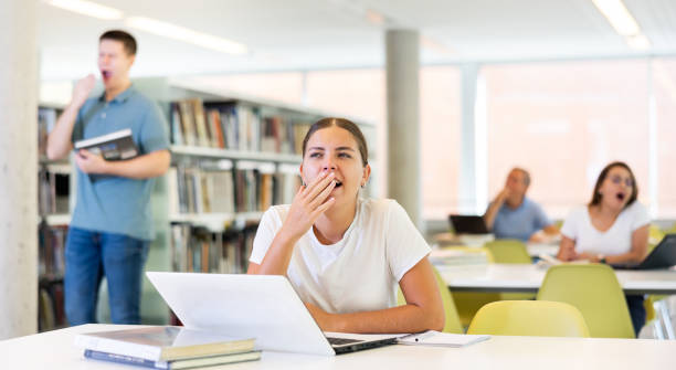 istock Young unproductive female remote worker yawning while working on laptop computer in the library 1454547011
