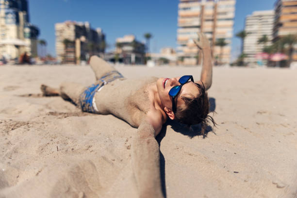 Teenage boy have fun rolling in sand on a beach on a sunny summer day. Canon R5