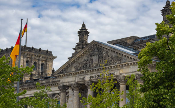 el edificio del reichstag, sede del parlamento alemán, el bundestag. la bandera alemana en un asta de bandera.  la entrada con la inscripción sobre los pilares. bandera alemana - berlin germany the reichstag german culture contemporary fotografías e imágenes de stock