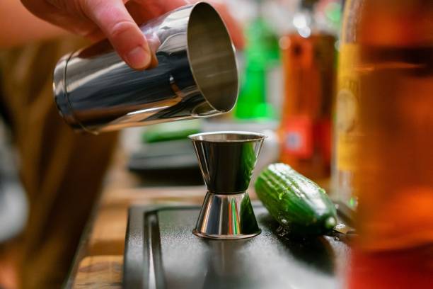istock Bartender making a cocktail with a shaker and a measuring cup next to alcohol bottles 1454551087