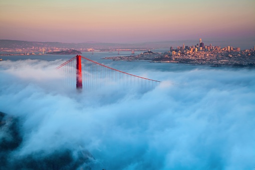 A beautiful drone shot of the top of golden gate bridge while it is hidden in the fog during sunset