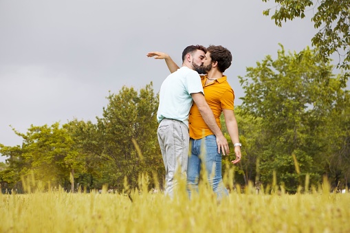 An adorable gay couple hugging and kissing in a park