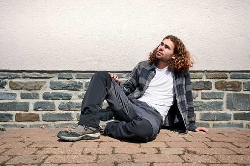 A Caucasian guy casually sitting on the ground of a street