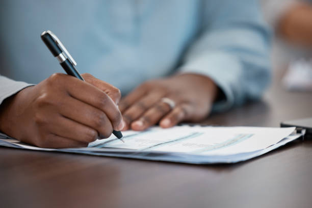 istock Hands, documents and contract with a black man signing paperwork at a table or desk in the office. Compliance, loan and insurance with a male putting his signature on a legal document for agreement 1454560346