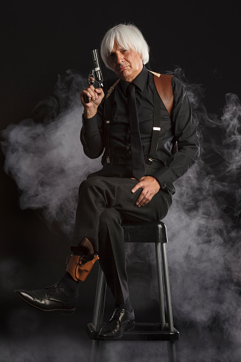 Vintage portrait of a senior man in black,  holding a gun. Cold and dangerous expression, deep look into camera.