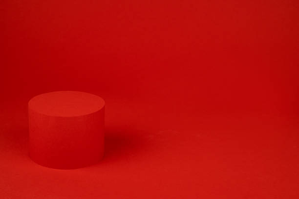 istock Red cylinder podium mockup on table on rich saturated background for presentation cosmetic products, gifts, goods in elegant minimal modern style, copy space. Template for advertising, design. 1454563290