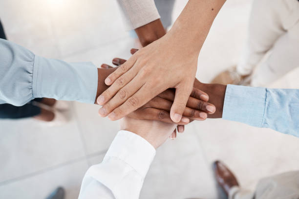 istock Hands, teamwork and motivation with business people standing in a huddle or circle together from above. Office, meeting and solidarity with a man and woman employee group joined in unity or trust 1454563546