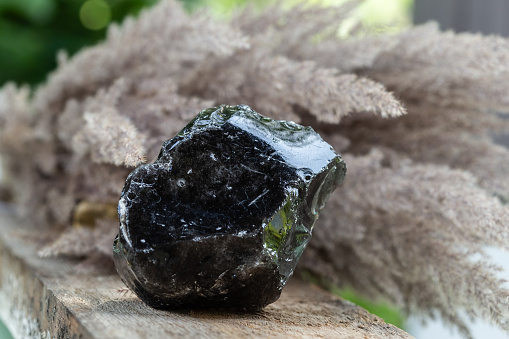 Black Obsidian Mineral Rock Sample over Wooden Background. Natural Volcanic Glass forms from Lava