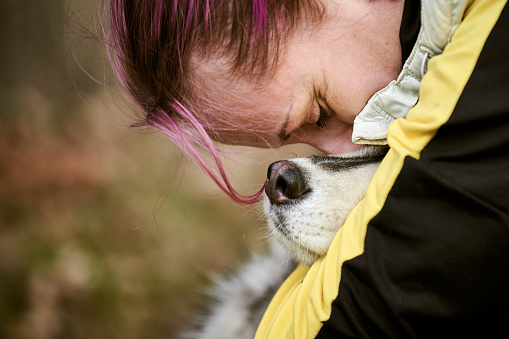 Woman with pink hair hugs Siberian Husky dog, true love of human and pet, funny meet of brown Husky dog and owner, left copy space. Girl hugging beloved Husky dog outdoor forest background
