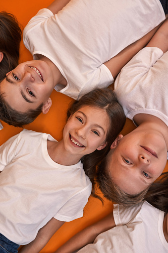 Partial top view of smiling caucasian children looking at camera. Boys and girls of zoomer generation. Modern youngster lifestyle. Friendship. Isolated on orange background. Studio shoot