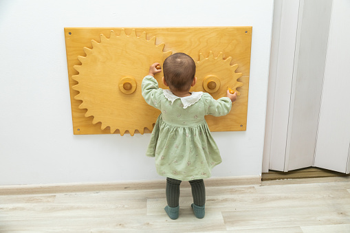 Toddler girl looking at wooden cogwheel busyboard in montessori space