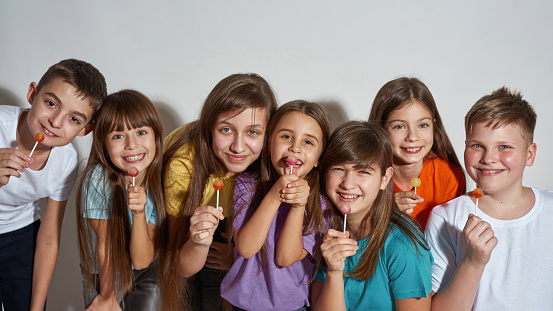 Group of smiling caucasian children posing with lollipops and looking at camera. Boys and girls of zoomer generation. Modern youngster lifestyle. Friendship. Isolated on white background. Studio shoot