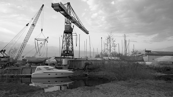 Crane from shipyard at industrial port with reflection of small white motorboat in water in Hard near Bregenz in Austria in black and white