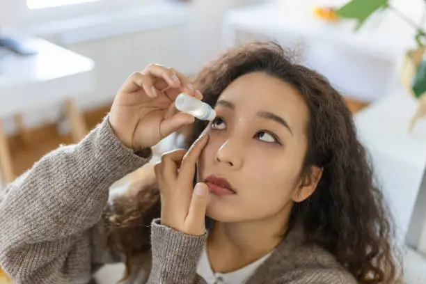 Asian Woman using eye drop, woman dropping eye lubricant to treat dry eye or allergy, sick woman treating eyeball irritation or inflammation woman suffering from irritated eye, optical symptoms