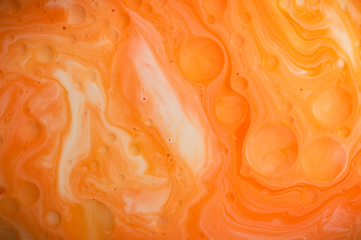 Macro close up depicting the abstract forms and shapes in a mixture of orange paint and oil.