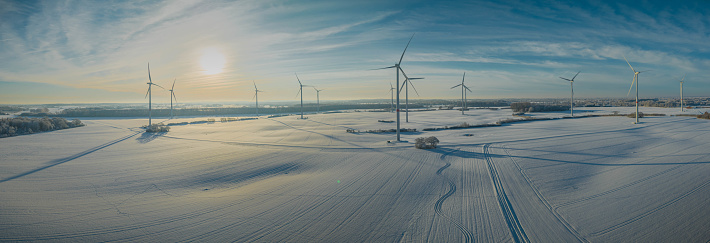 The winter snow on a rural agricultural field with view of wind turbine in the background. Snowy white frozen agricultural field in the countryside and wind turbines.