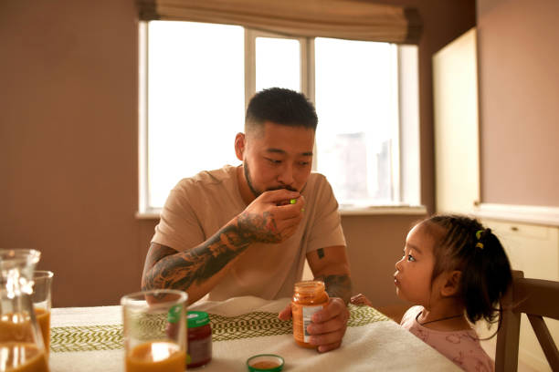 dziewczyna patrzy na ojca jedzącego jedzenie dla niemowląt łyżką - sparse healthy eating single father contemporary zdjęcia i obrazy z banku zdjęć