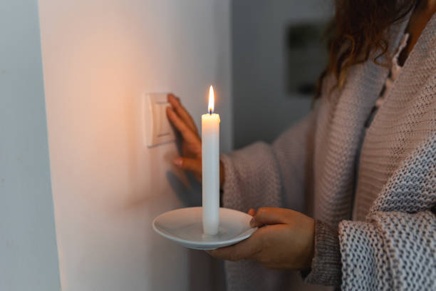 istock Energy crisis. Hand in complete darkness holding a candle trying to turn on light during a power outage. Blackout concept. 1454583253
